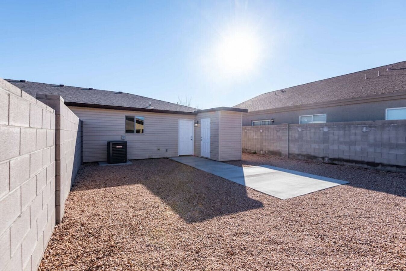 Un jardin à l’arrière d’une maison, avec une terrasse en béton, un garage et une allée gravillonnée.