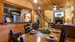 A wooden interior with a dining area, a fireplace, and a staircase. - Forward My Calls · Elevate Your Stay: 4 Decks, Hot Tub, & Idyllic Outdoor Haven (Broken Bow)