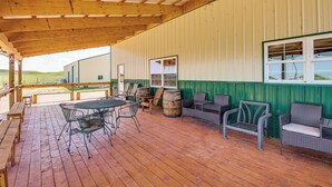 Un patio techado al aire libre con suelo de madera, mobiliario de metal y mimbre, y vistas del paisaje circundante.
