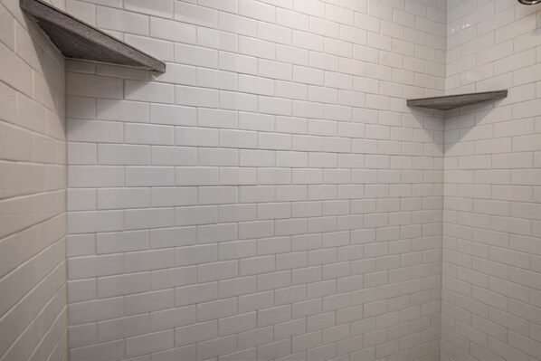 Un espace douche avec des murs recouverts de carreaux blancs et des accessoires en métal.