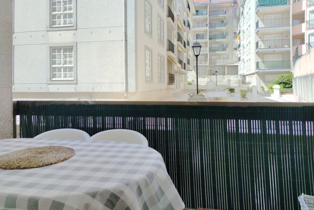 Habitación de hotel con una colcha a cuadros, un mantel tejido y vista a un edificio de varios pisos con balcones.