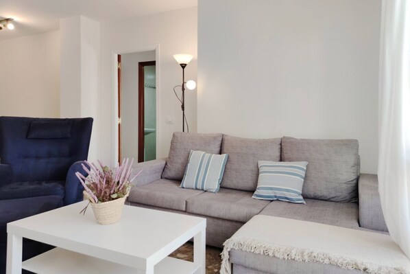 Un salon avec un canapé gris, un fauteuil bleu, une table basse blanche et un lampadaire.