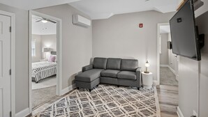 A modern living room with a gray sectional sofa, a flat-screen TV mounted on the wall, and a patterned rug on the floor.