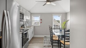 A modern kitchen with stainless steel appliances, a dining area with a table and chairs, and a ceiling fan.