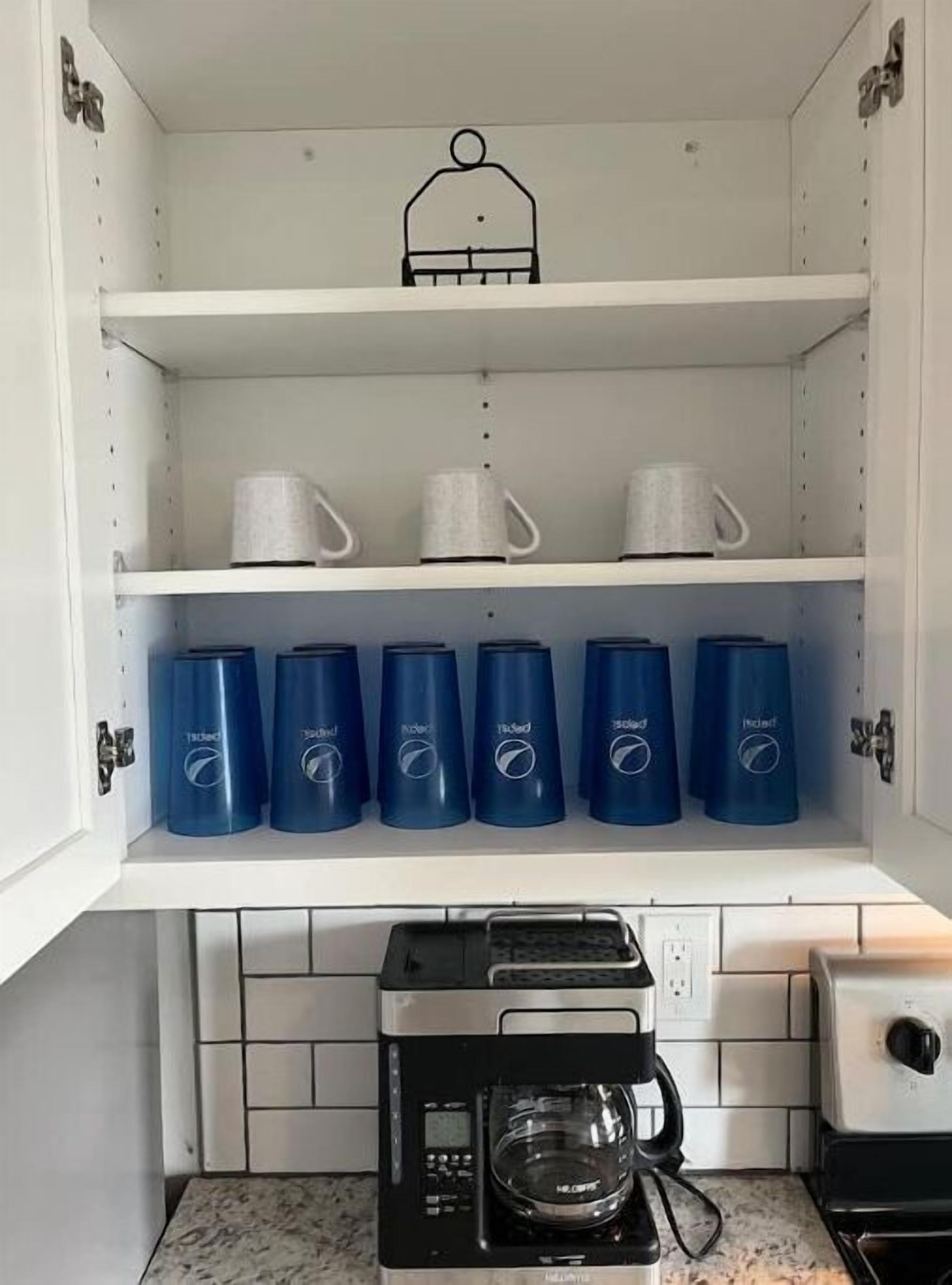 Une cuisine avec des meubles blancs, une machine à café et six récipients bleus sur l’étagère du milieu.