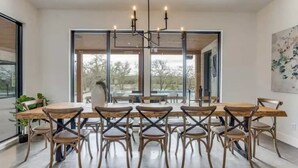 Un espace repas avec une longue table en bois et des chaises, de grandes fenêtres et un lustre moderne.