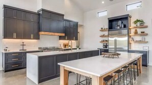 Une cuisine moderne avec des meubles de couleur sombre, un grand îlot central doté de tabourets et des appareils électroménagers intégrés.