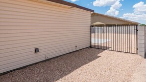A building with a beige exterior, a gravel driveway, and a black metal gate. - Brand New Duplex! Minutes from every amenity! (Kingman)