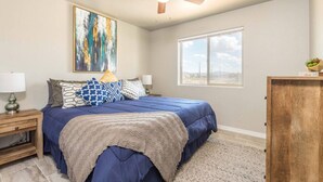 A bedroom with a bed, a ceiling fan, a window, and a painting on the wall. - Brand New Duplex! Minutes from every amenity! (Kingman)