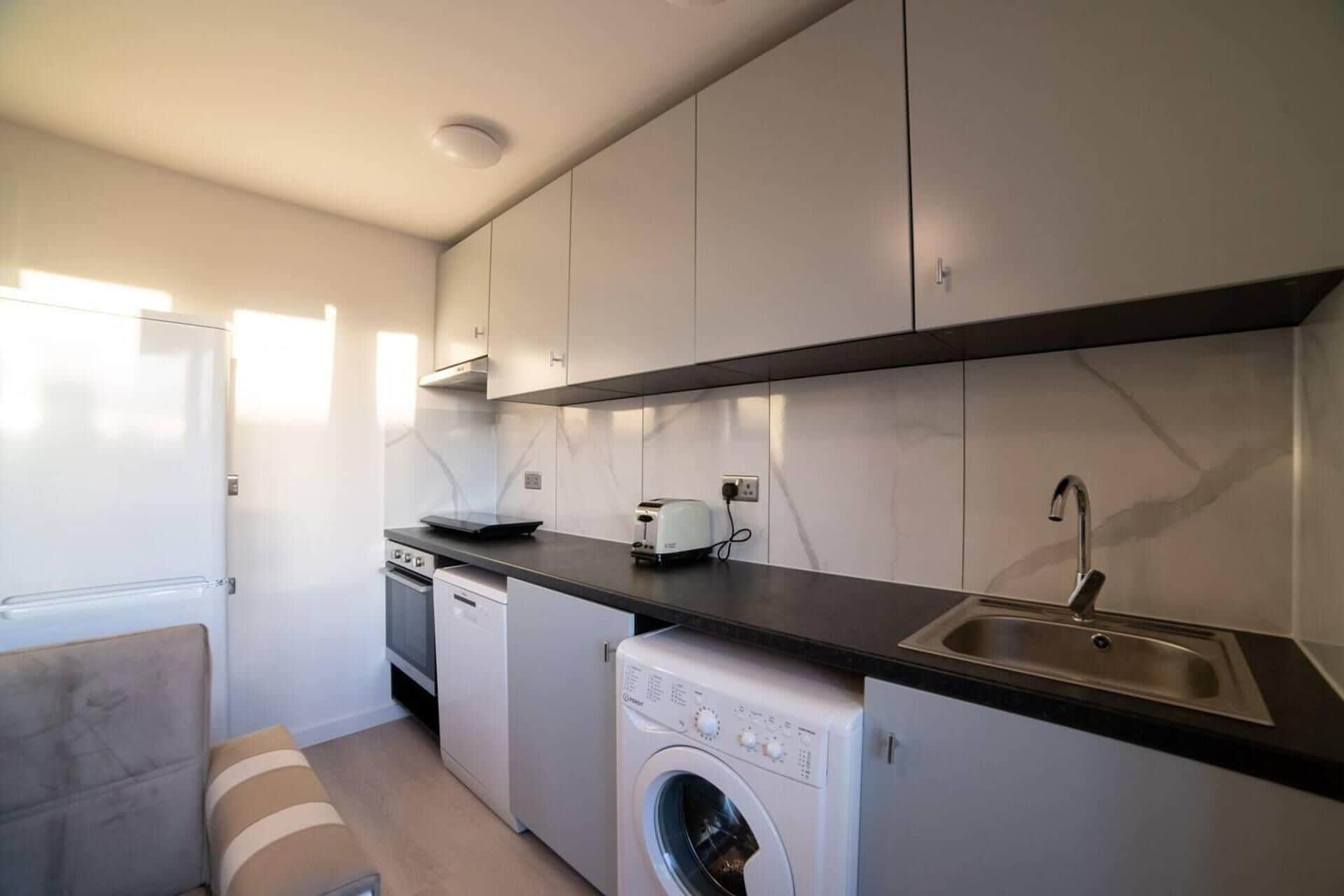 A compact kitchen with a dishwasher, washing machine, and a sink.