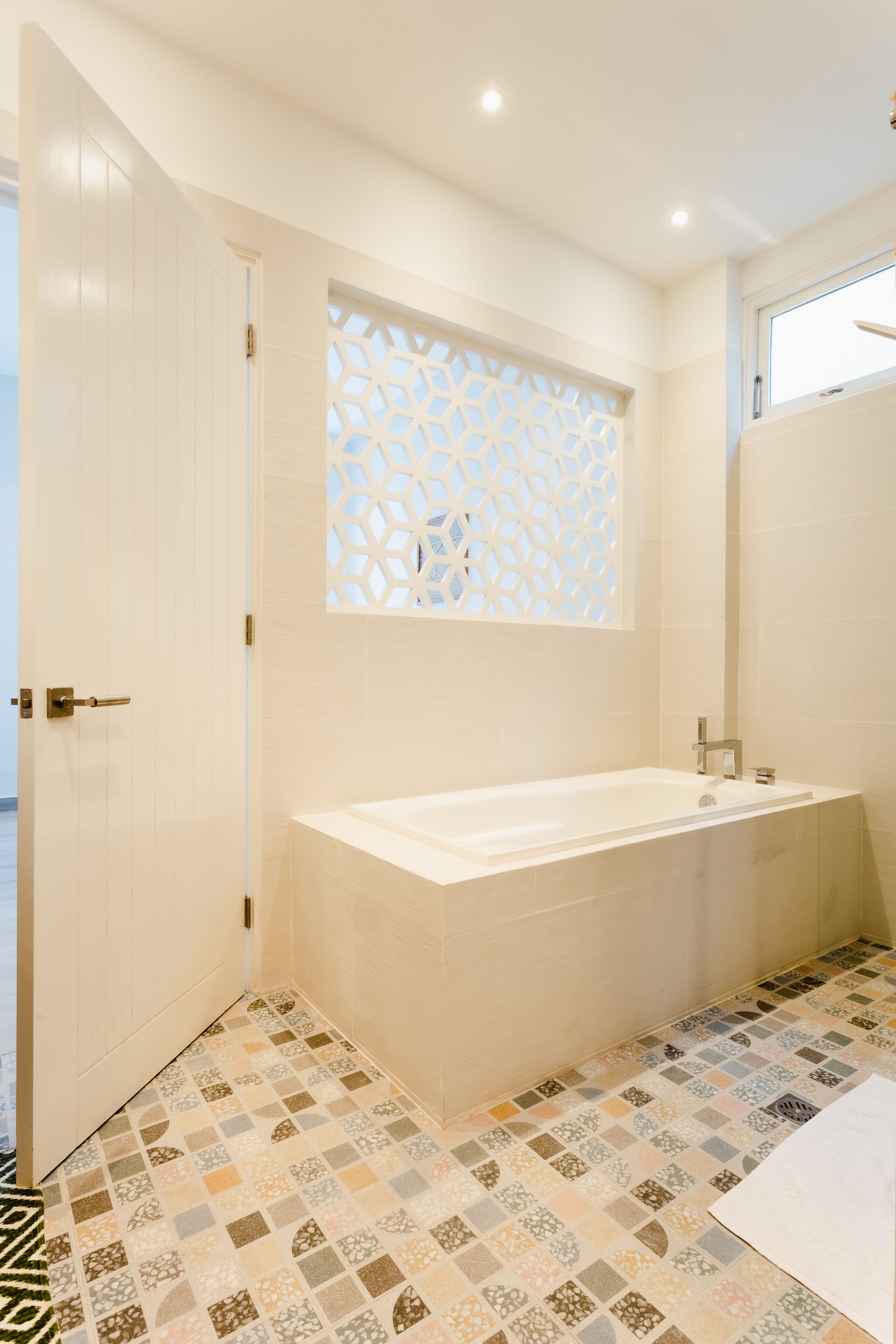 Un baño moderno con una bañera independiente, un ventanal decorativo y baldosas estampadas en el suelo.