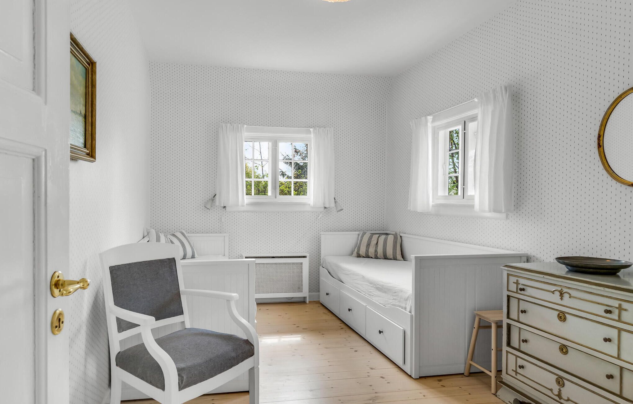 Habitación compacta y bien iluminada con una paleta de colores blanco y gris, que incluye un sofá, una silla, una mesita y un aparador.