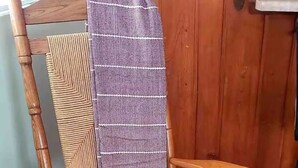 Een houten schommelstoel met een geweven zitting en rugleuning, geplaatst in een kamer met houten vloeren en een houten deur op de achtergrond.