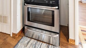 Een kleine keuken met een RVS fornuis en oven, witte muren en een houten vloer.