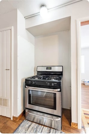 A compact kitchen with a stainless steel stove and oven, white walls, and a wooden floor.