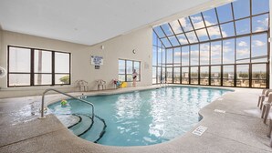 An indoor swimming pool with clear glass walls, a lifeguard sign, and a view of the sky.