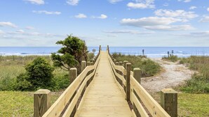 A wooden boardwalk leading to a beach with a clear sky and a few clouds.