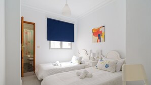 Ein Hotelzimmer mit zwei Betten, einem Badezimmer und einem Fenster mit blauer Jalousie.