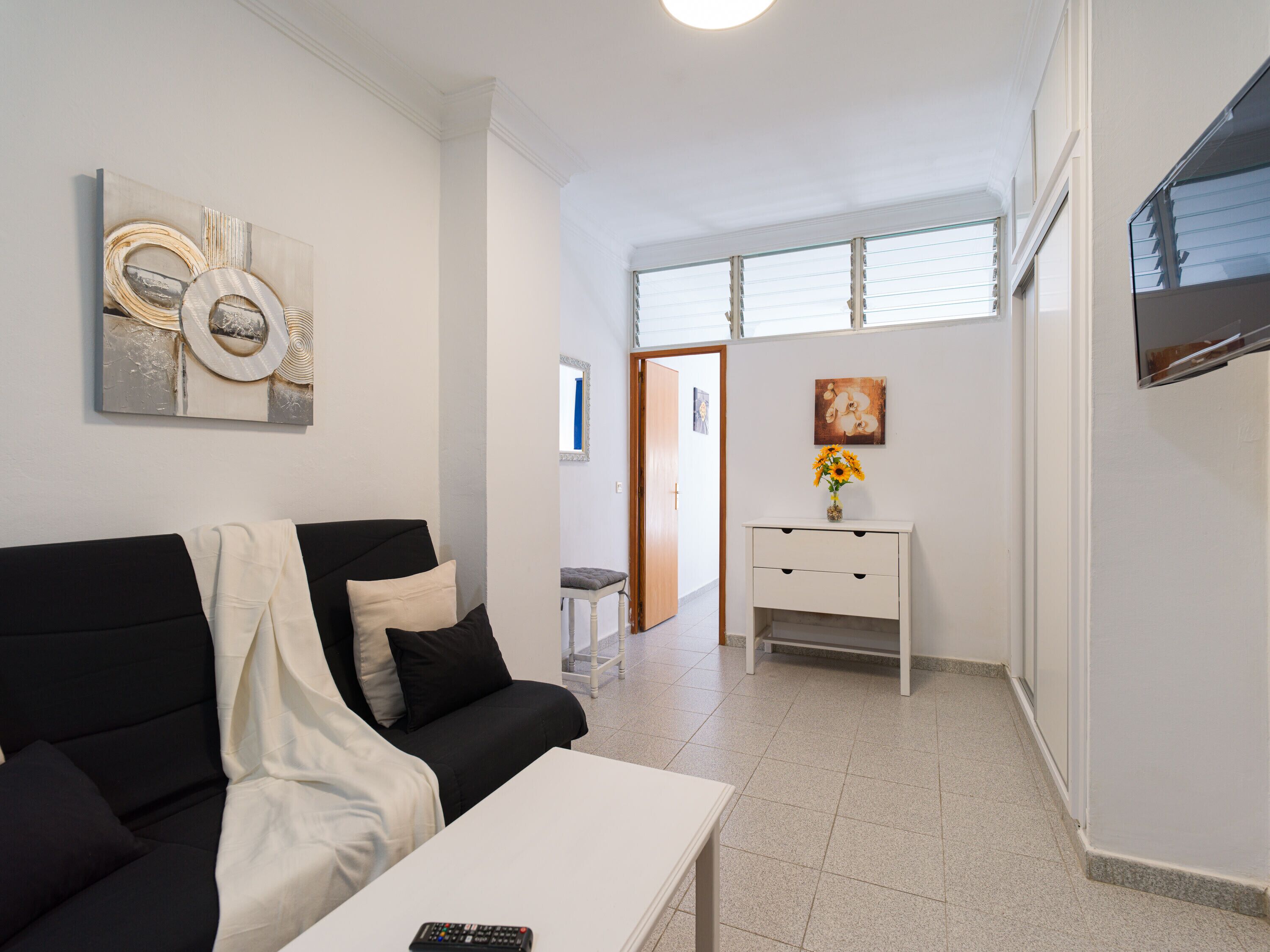 A modern living room with a black sofa, white coffee table, and a white console table with a vase of flowers.