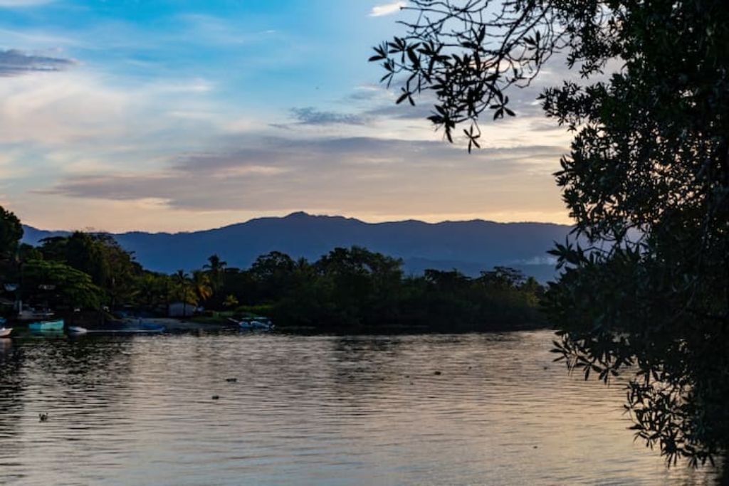 Um lago tranquilo com montanhas ao fundo e alguns barcos na água.