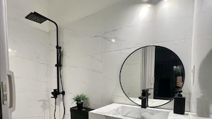 Een moderne badkamer met een zwart toilet, een wit marmeren wastafel, een ronde spiegel en een douchekop.