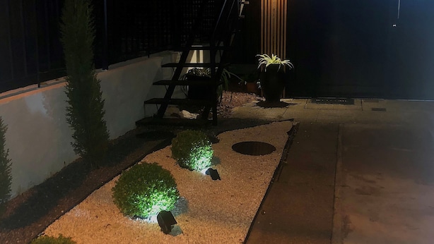 Een buitenruimte 's nachts met een pad, plantenbakken en een trap die naar een gebouw leidt.