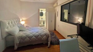 Een slaapkamer met een bed, een kledingkast, een spiegel, een raam en een televisie.