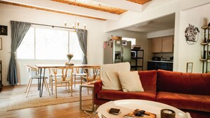 A living room with a red sofa, a dining table with chairs, a kitchen in the background, and a large window with curtains. - Good Life Cabin- EV-Hot Tub-Lake Access-Pups OK (Arnold)