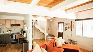 A modern kitchen with a stove, oven, and sink, a wooden staircase, and a living area with a red sofa and cushions. - Good Life Cabin- EV-Hot Tub-Lake Access-Pups OK (Arnold)