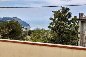 A coastal view with a mountain, trees, and a building with a tiled roof.