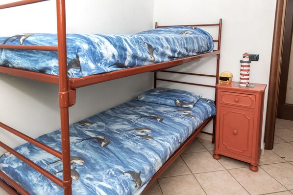A bunk bed with a blue ocean-themed bedspread, a small wooden cabinet, and a toy lighthouse.