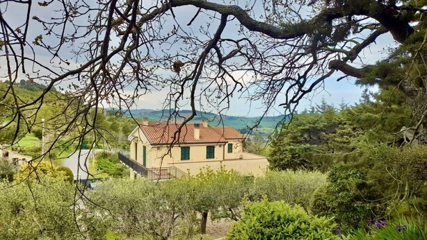 Une maison avec un toit recouvert de tuiles rouges, entourée de verdure et d’arbres.