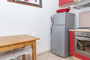 A compact kitchen with a refrigerator, oven, and a wooden table with chairs.