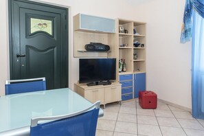 A room with a glass table, blue chairs, a television, a cabinet with shelves, and a red suitcase. -  A27 - Poggio, four-room apartment with sea view on ​​Portonovo Bay (Ancona)