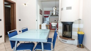 Un coin repas avec une table en verre et des chaises bleues, une cuisine équipée d’une cuisinière et d’un four, et une cheminée.