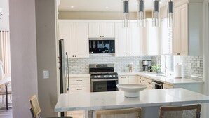 Cocina moderna con armarios blancos, electrodomésticos de acero inoxidable y una isla central con taburetes de bar.