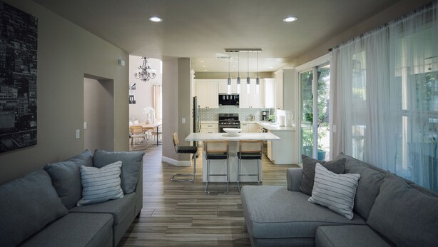 Una sala moderna con un sofá gris, una mesa de centro y una cocina con armarios blancos y una isla central.