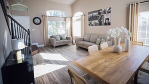 Amplia sala de estar con una mesa de comedor de madera, dos sofás, una escalera y un candelabro.