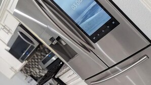Une cuisine moderne dotée d’appareils électroménagers en acier inoxydable, d’une horloge numérique et d’un design épuré.