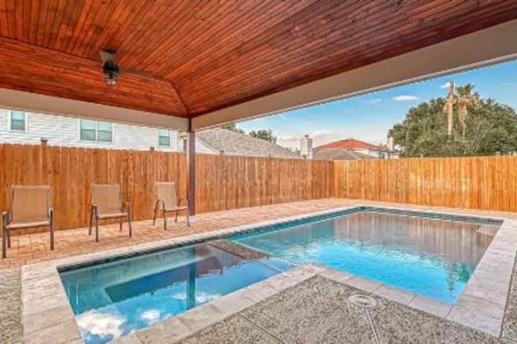 Une piscine rectangulaire avec une terrasse en bois et des chaises, entourée d’une clôture en bois.