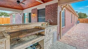 Un espace cuisine extérieur avec un mur en briques, un ventilateur de plafond et un barbecue.