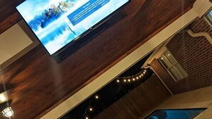 Un intérieur moderne avec un grand téléviseur à écran plat fixé à un mur en bois, un espace piscine doté d’un design géométrique original et un mur de briques avec une fenêtre.