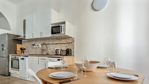 A modern kitchen with white cabinets, a microwave, and a dining area with a wooden table and white chairs.