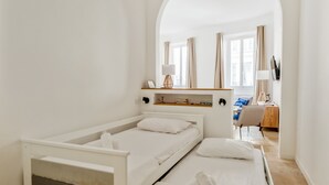 A hotel room with two single beds, a desk with a chair, a mirror, and a window with curtains.