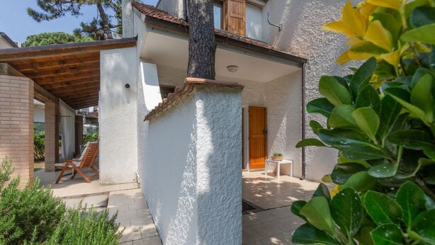 A house with a covered patio, a wooden door, and a small table with a plant. - Villa with garden on two levels (ground floor and first floor) with internal stairs.In 70 square meters of space, it comfortably accommodates 6 people with two bedrooms (one with a double bedroom, one with two single beds) and a double sofa bed in the li (Lido di Spina)