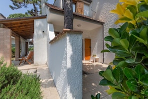 A house with a covered patio, a wooden door, and a small table with a plant. - Villa with garden on two levels (ground floor and first floor) with internal stairs.In 70 square meters of space, it comfortably accommodates 6 people with two bedrooms (one with a double bedroom, one with two single beds) and a double sofa bed in the li (Lido di Spina)