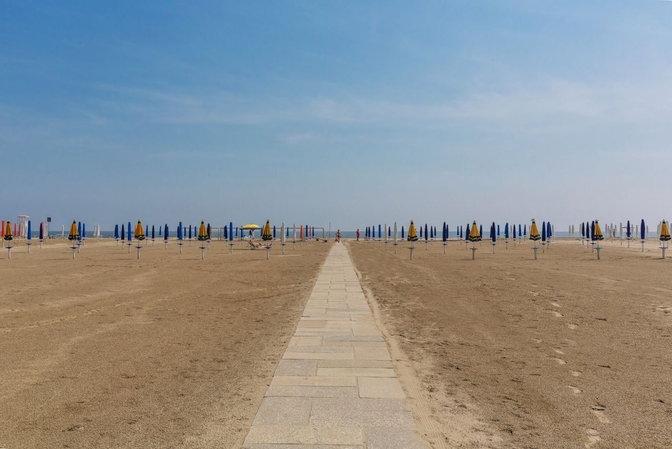 A beach with a central pathway, umbrellas, and beach chairs arranged in rows.