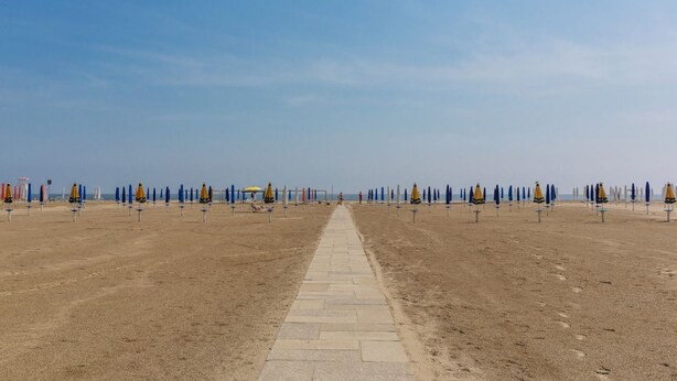Una playa con un camino central, sombrillas y sillas de playa dispuestas en filas.