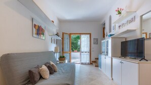 A modern living room with a grey sofa, a flat-screen TV, and a kitchen area with cabinets and a countertop. - Villa with garden on two levels (ground floor and first floor) with internal stairs.In 70 square meters of space, it comfortably accommodates 6 people with two bedrooms (one with a double bedroom, one with two single beds) and a double sofa bed in the li (Lido di Spina)