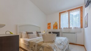 Un dormitorio con cama, mesita de noche, lámpara, radiador, ventana y una obra de arte.